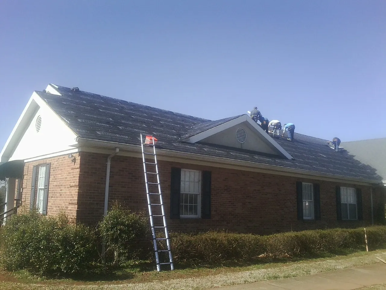 Crew tearing shingles off a brick ranch roof with a ladder set — Metal Roof Repair work by our crew in Minersville