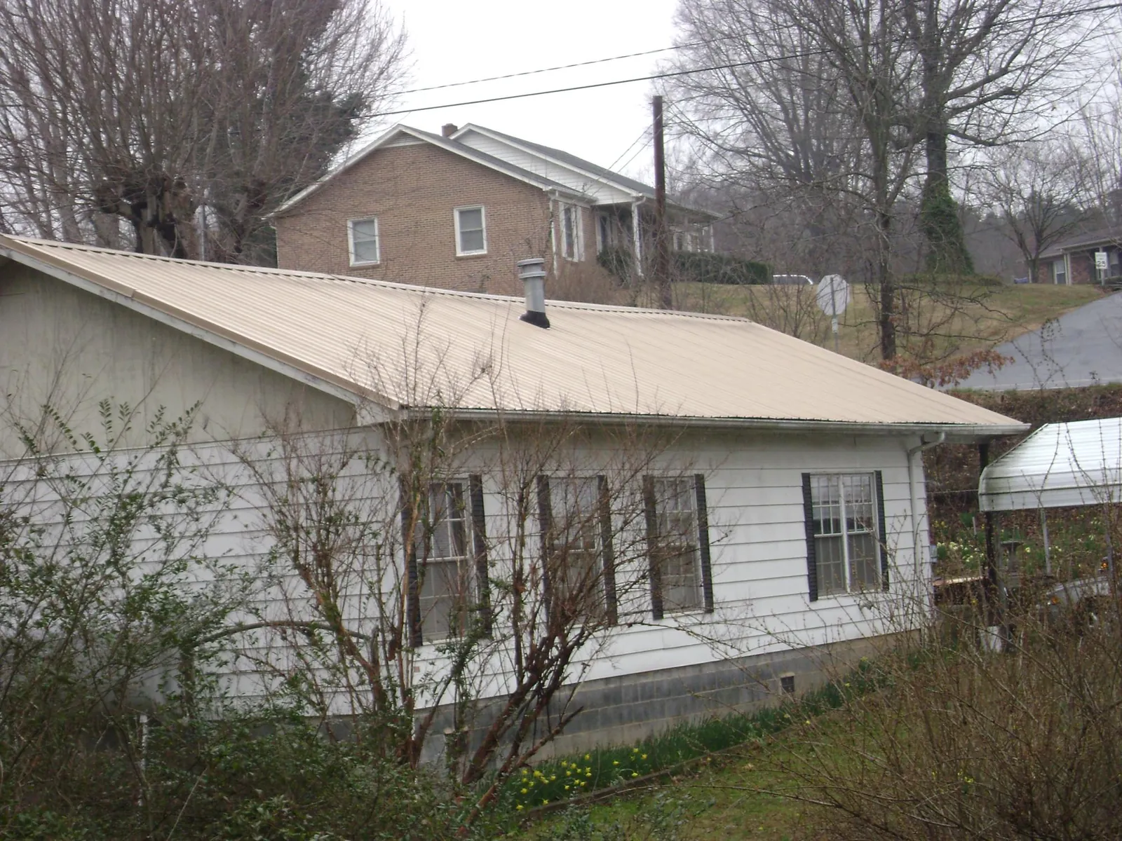 Tan metal roof on a white sided house set into a hillside — Commercial Roofing by Roofing Brothers in Minersville